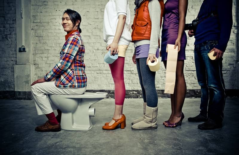 happy eccentric guy on the toilette while a line of people waits for their turn-cm