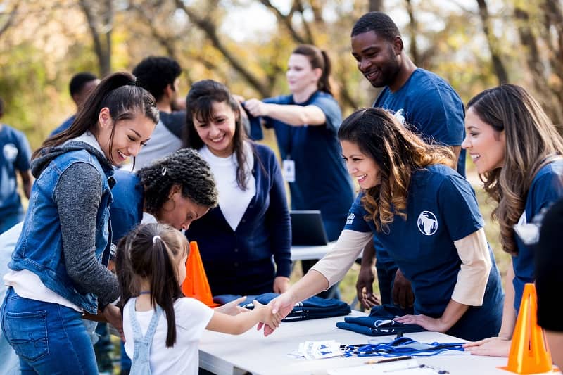 Mid adult volunteer shakes hands with girl at registration table-cm