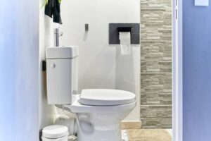 Intelligent white toilet with a washbasin on top, a wastebasket next to it and toilet paper on the wall, seen from the bathroom entrance. -cm