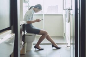 Woman sitting on flush toilet typing smartphone-cm